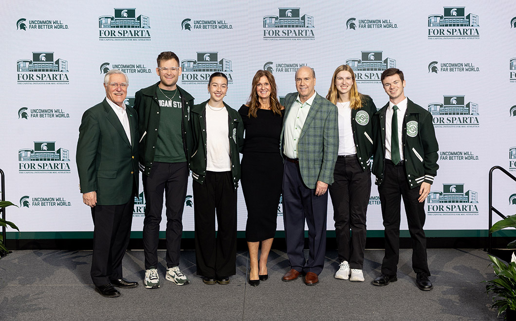 a row of seven people stand side by side while smiling