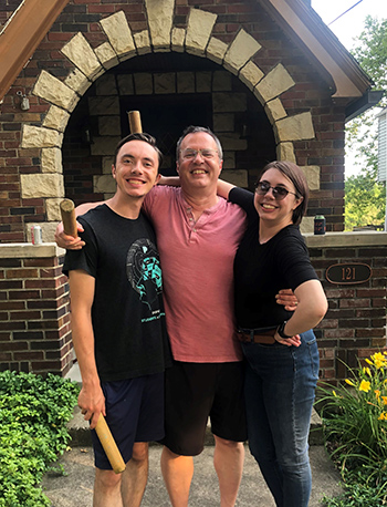 three people stand and smile in front of the front door of a house