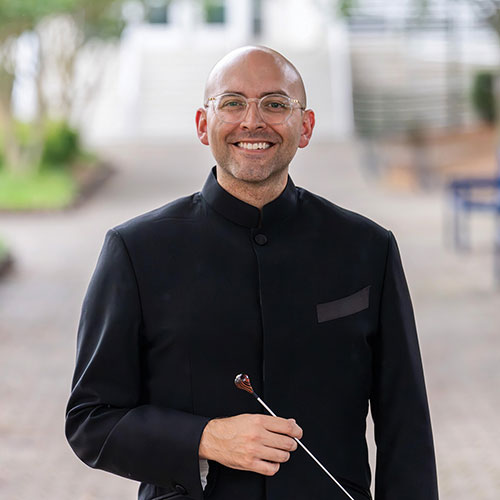 Conductor Tyler Austin poses for a photo. He smiling, looking at the camer and holding a baton