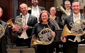 group of people on a stage all holding French horns