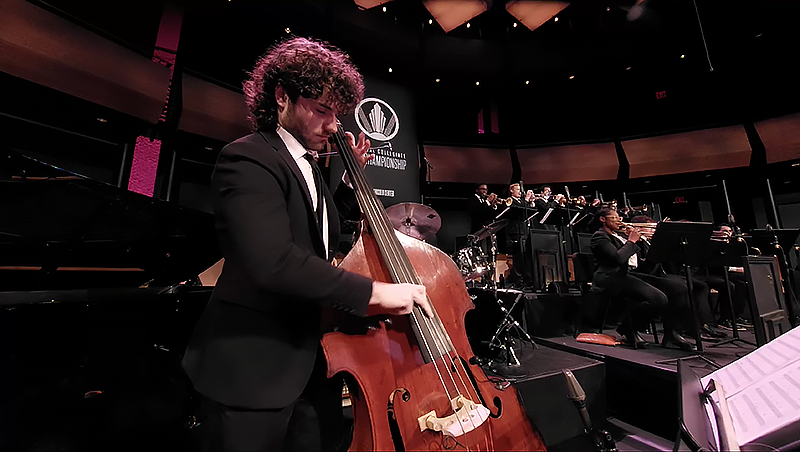 person plays upright bass on stage with other musicians in the background