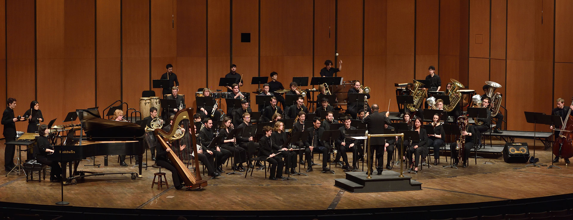 MSU Wind Symphony ensemble musicians, full stage with several instrumentalists performing, conductor leading ensemble in the foreground.