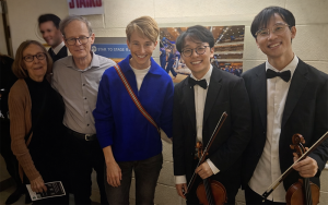 group of five people together, two holding violins