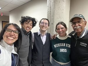 five people standing shoulder to shoulder while smiling