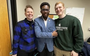 three people standing shoulder to shoulder while smiling