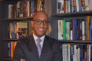 a smiling person with standing in front of full bookshelves