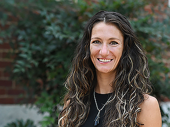 a smiling person outside of an ivy covered wall