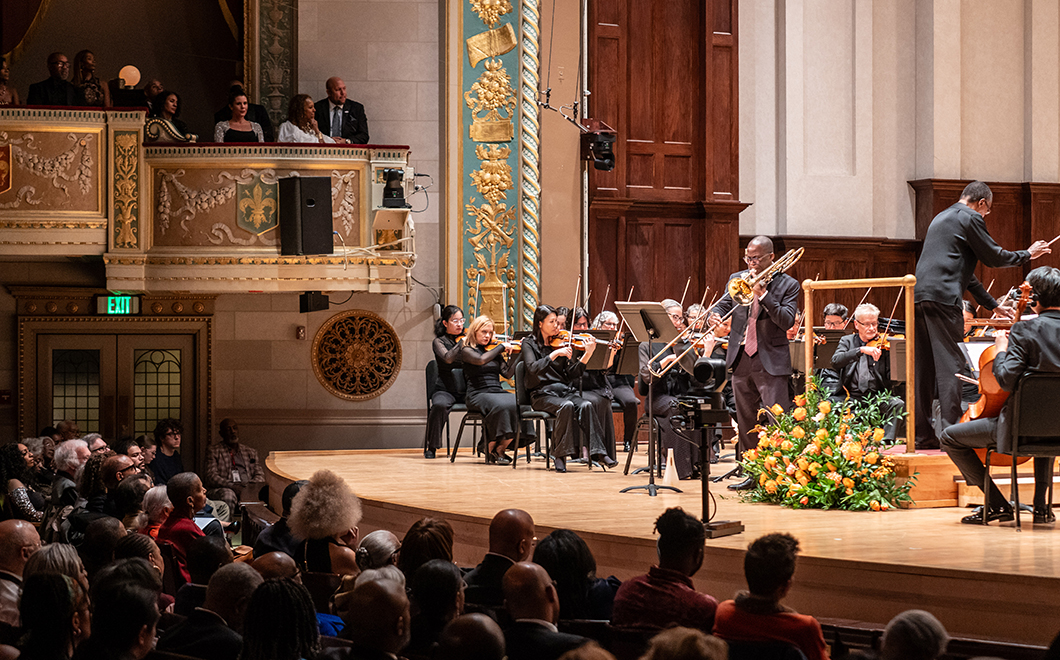a person on stage performs on trombone with an orchestra