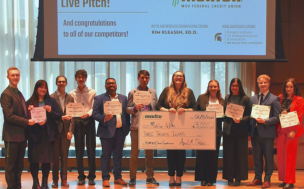 a group of 11 people standing in a row in front of a large presentation screen, all holding certificates