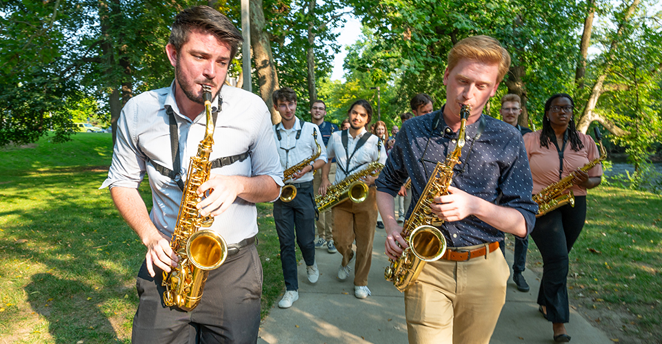 a group of saxophone players play as they walk down a sidewalk