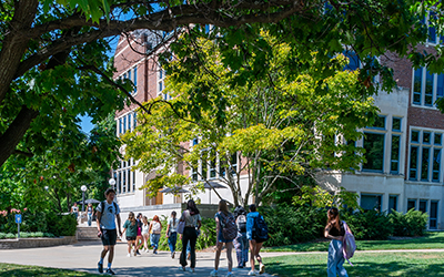students walking outside near trees and a brick building