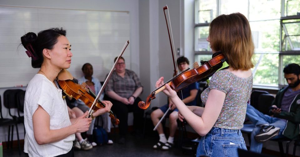 violin teacher works with students