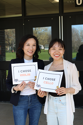 two people holding printed signs that say I chose violin and I chose cello