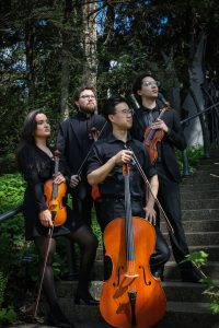 Image of the Mirana String Quartet holding their instruments, posed outside in a natural landscape with trees in the background.