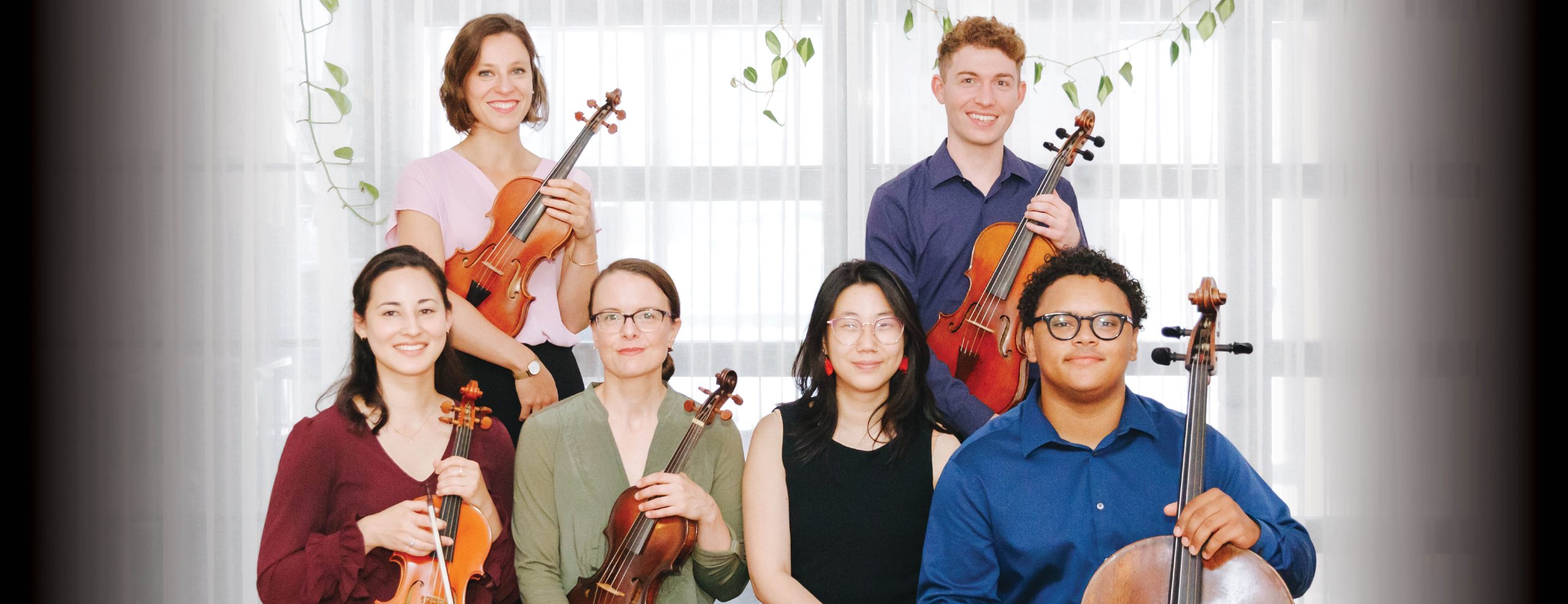 Image shows guest ensemble holding their instruments, posed for a photo. There are 4 people in the front row, and 2 in the back. The background shows white curtains with some hanging leaves.