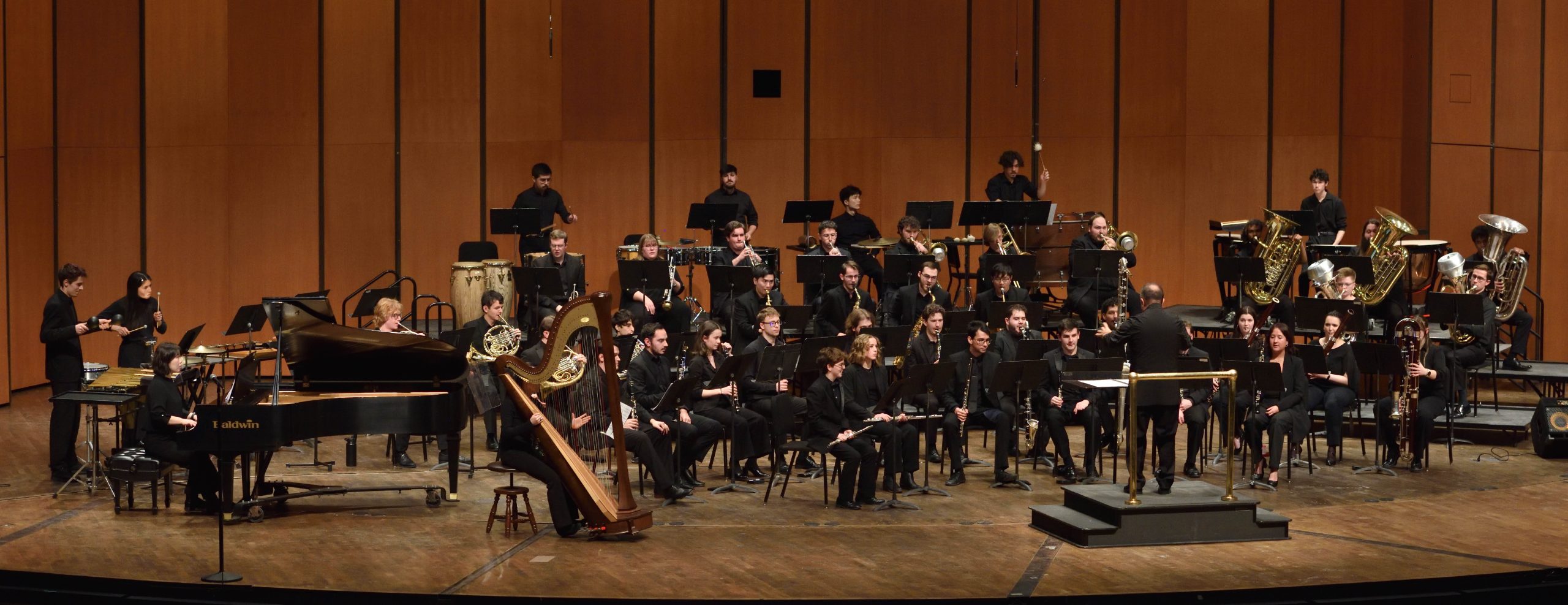 Wide image of Wind Symphony performing on stage. Conductor in the center.