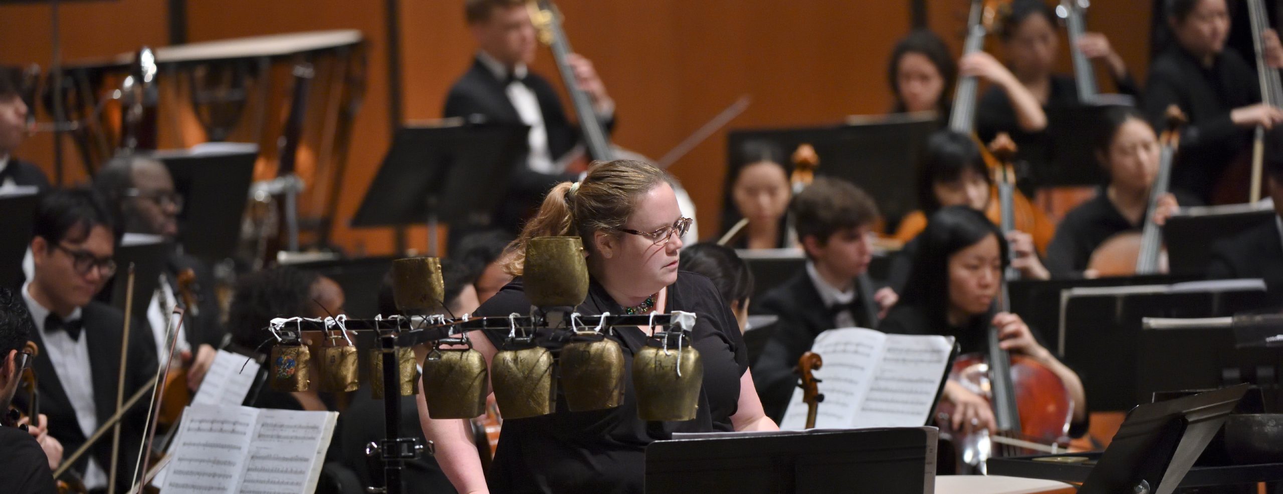 Foreground shows guest artist and percussion instruments. Background shows MSU string players with their instruments, performing on stage.