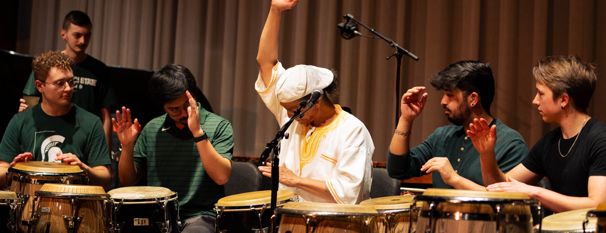 African Diaspora Percussion Ensemble performing on stage. Five individuals playing drums.