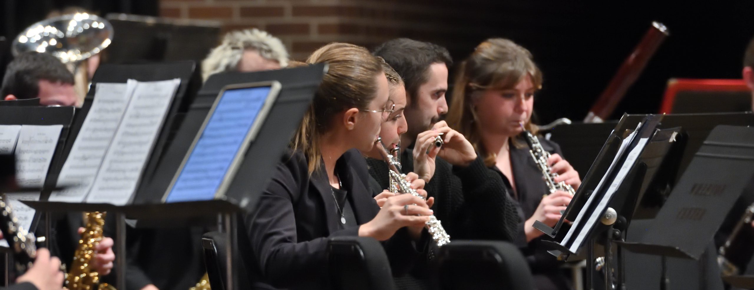 Close up of MSU flute players performing on stage with their instruments, in front of music stands.