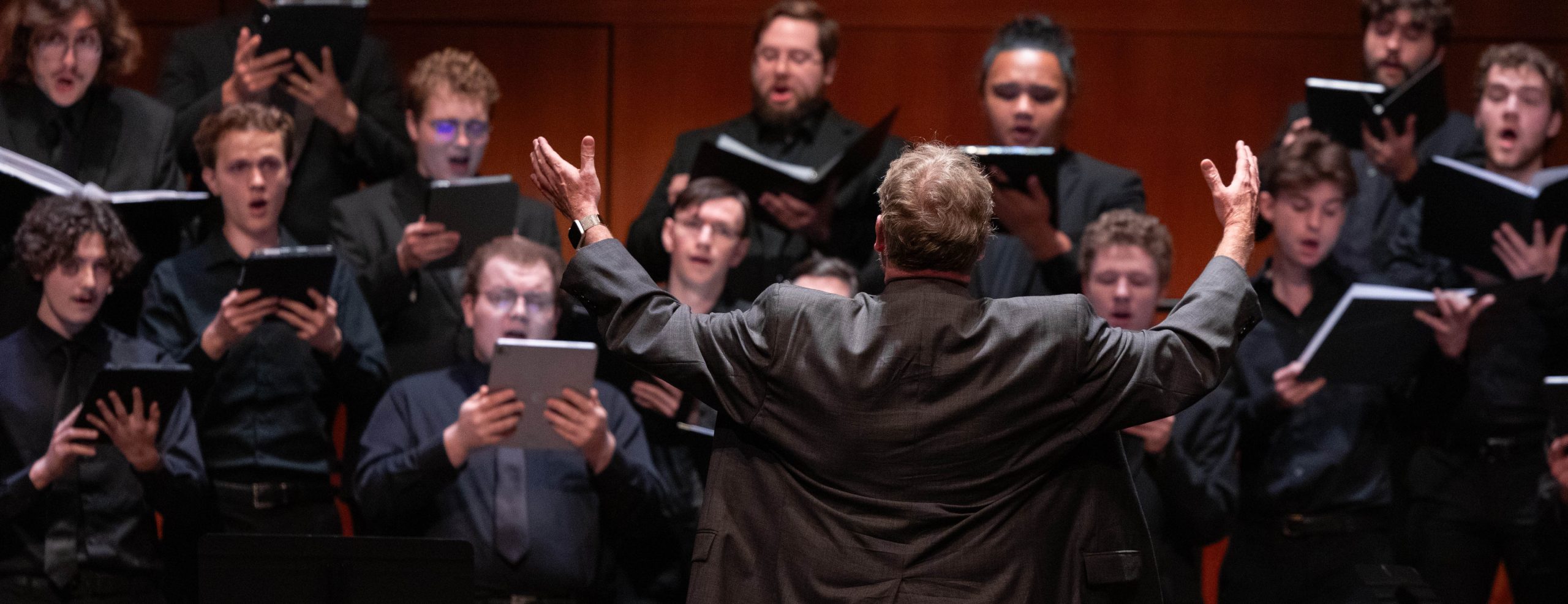A choir dressed in all black performing on stage in front of a conductor