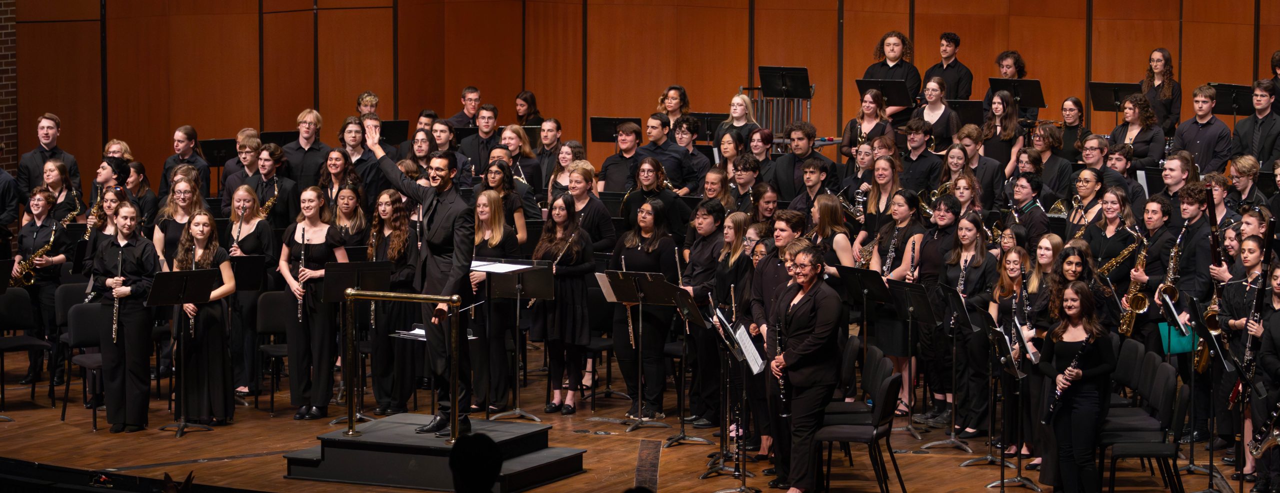 Wide image of MSU Band on stage standing with their instrument for bows.