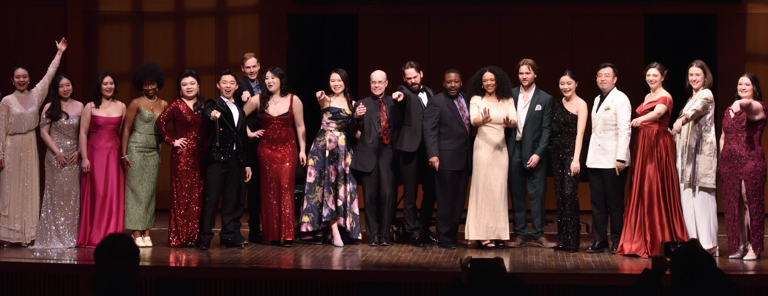Image shows vocal artists singing together on stage, dressed in formal attire.