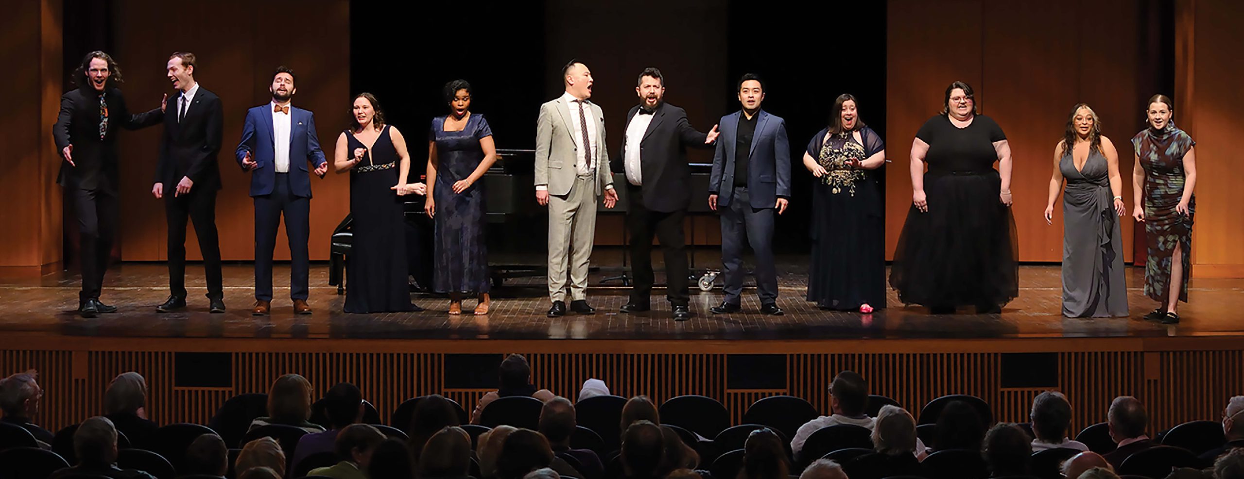 Image shows 7 vocal artists singing together on stage, dressed in formal attire.