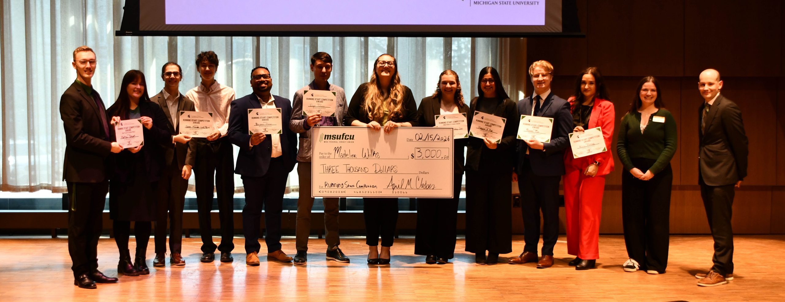 12 individuals stand for a photo with award certificates. The middle of an image shows the recipient of a big check.