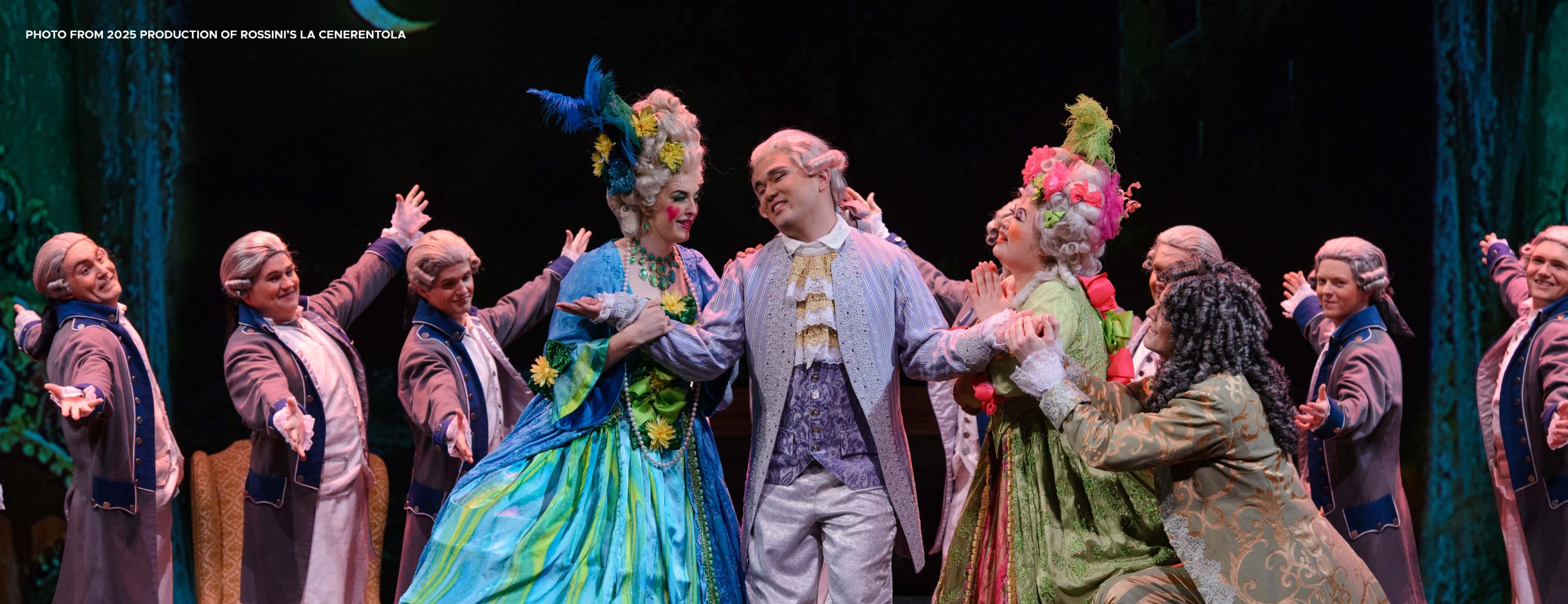 Image from MSU's 2025 production of Rossini's La Cenerentola. Image shows 4 people in costume in a tableau in the center of the stage. The background shows a male chorus in costume.