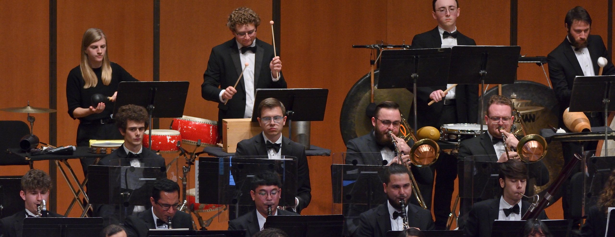 Image shows MSU percussion, brass and woodwind players playing isntruments on stage in front of music stands.