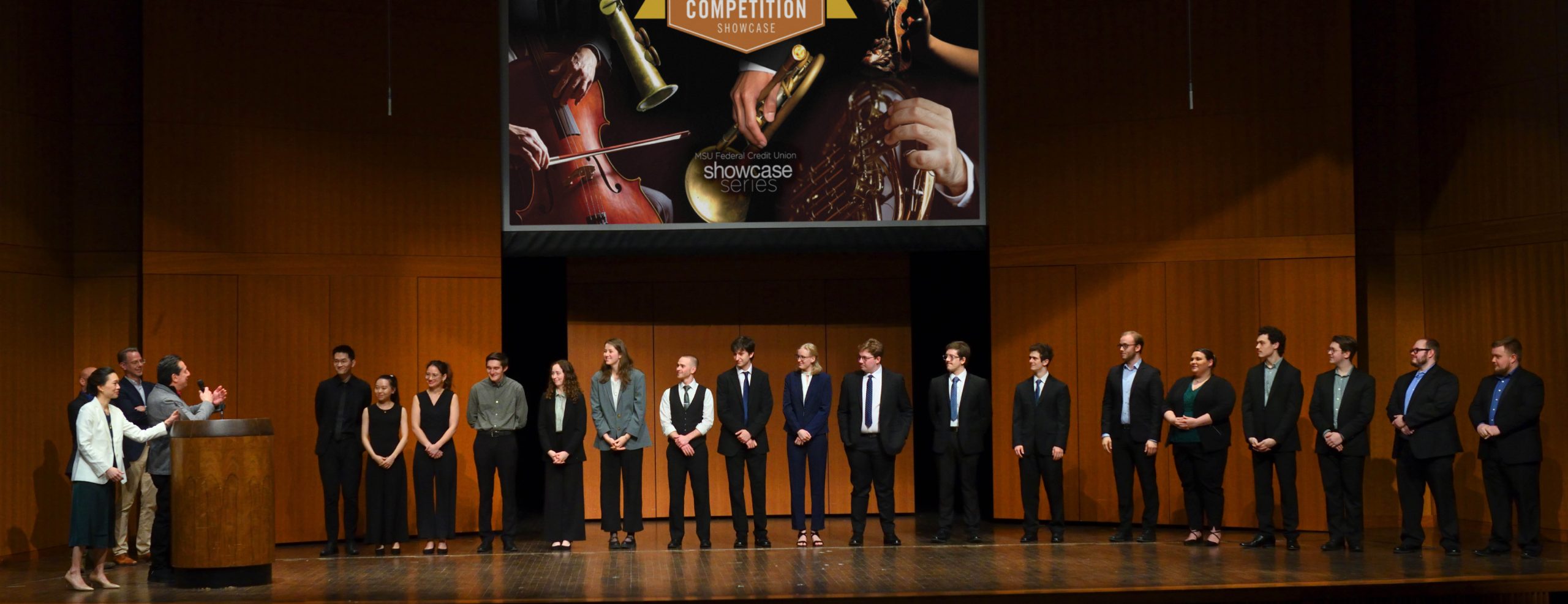 Chamber Music competition awards presentation with instrumentalists on stage and judges commenting on performance, promotional graphic projected on screen that has event title and closeup of instruments