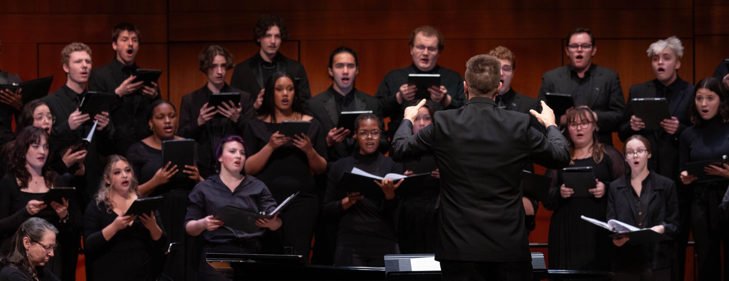 A choir dressed in all black performing on stage in front of a conductor
