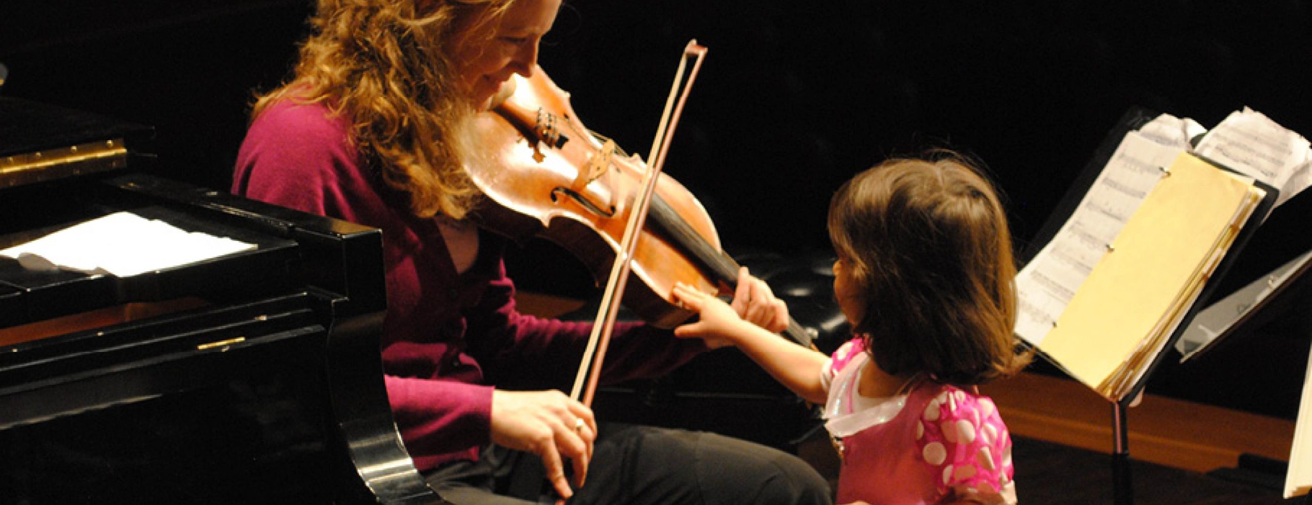 Sensory Friendly Spartan Concert. Woman playing stringed instrument for young child on stage.