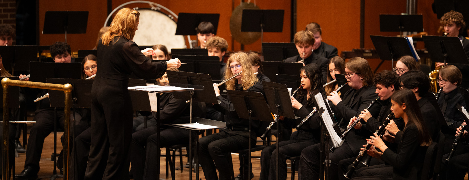 Youth wind symphony musicians performing on stage led by conductor