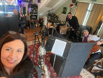 a person in the foreground takes a selfie with musicians recording in a studio