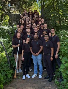 Group picture in outdoor setting of conducting symposium participants. All weaing same black event shirts and standing at stairwell