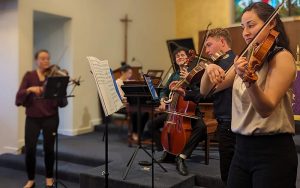 Baroque era music ensemble in a performance setting staged within a church and showing string musicians.