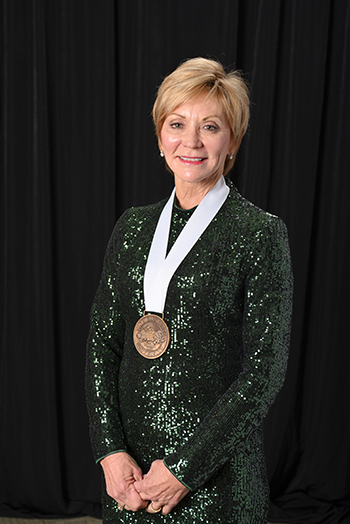 a person in a green dress wearing a white ribbon with a an award medal