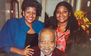 two people stand behind and older person, all are smiling