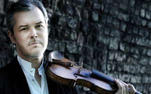 Photo portrait, violinist, serious facial expression, holding violin up to shoulder, looking at camera.